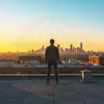 Confident figure overlooking sunrise cityscape, symbolizing underdog triumph and fresh business beginnings.